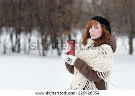 Young beautiful woman with metallic tumbler walking in winter park