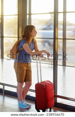 Young woman with suitcase at the airport with airplane on background