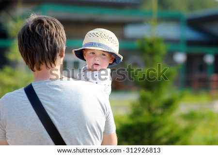 Middle age father with his toddler son walking outdoors at the hot summer day