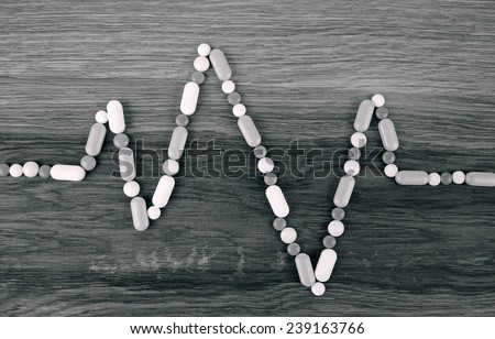 Heart rate graph line made from pills placed on wooden background monochrome