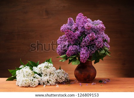 Purple lilacs in a vase and white lilac on the table