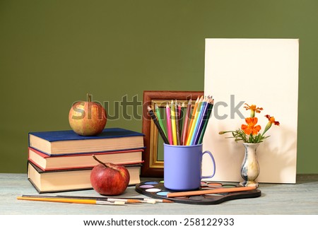 Books, apples, colored pencils and painting canvas on the table