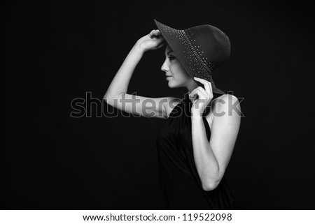A black and white studio portrait of lovely black dress and black hat over dark background on Beauty and Fashion theme