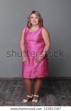 Female portrait of charming woman wearing bright pink elegant dress over gray background