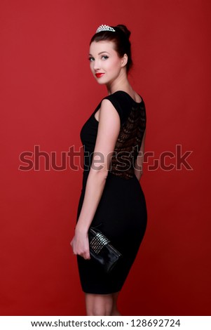 Smiley girl posing over red background/Beautiful figure of a girl in black dress on Holiday