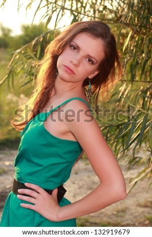 Charming sad young woman with dark long hair in a summer dress in the park on Beauty and Fashion