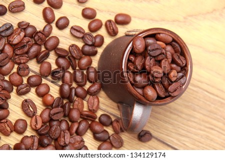 Top view on dark brown coffee beans in small ceramic coffee cup over light brown wooden background