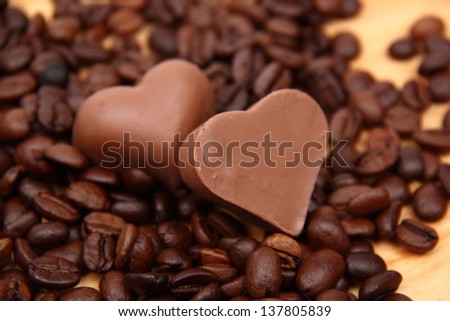image of chocolates in the form of heart with lots of coffee beans over light brown wooden background