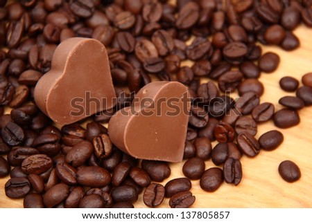 Chocolates in the form of heart with lots of coffee beans over light brown wooden background