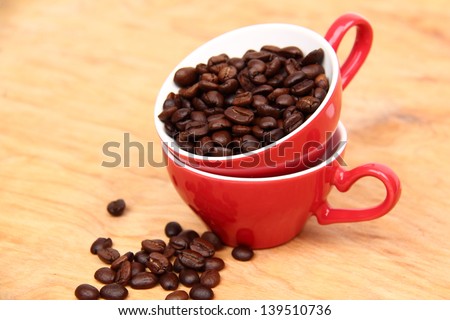 Coffee beans in red ceramic coffee cup with heart symbol on wooden background