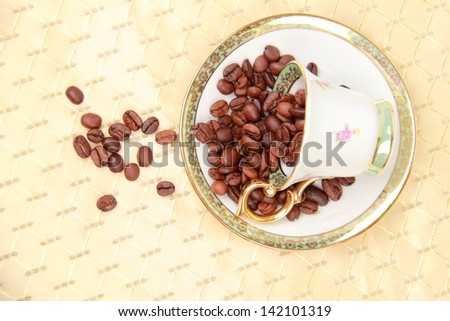 White coffee cup full of coffee beans on the beige tablecloth on Food and Drink