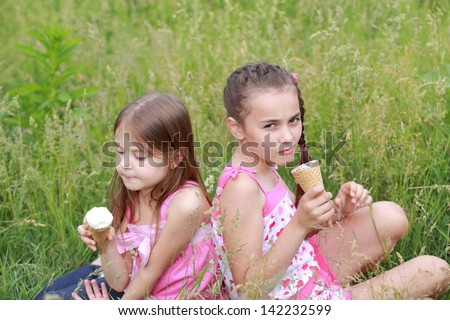 Charming two young girls eat ice cream and lie on the grass outdoors