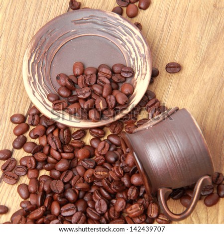 Delicious dark brown coffee beans in small ceramic coffee cup over light brown wooden background