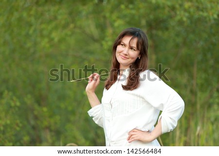 Charming caucasian woman with a sweet smile in white dress standing in a field in the countryside