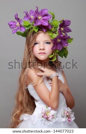 Caucasian cute little girl with beautiful hairstyle with fresh bright clematis smiles and poses for the camera