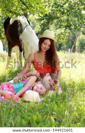 Image of a happy family in a summer garden with a charming ponies / Young mother with young children resting on the green grass in the apple garden