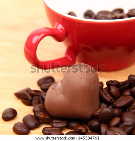 Coffee beans in red ceramic coffee cup with heart symbol and yummy chocolate heart
