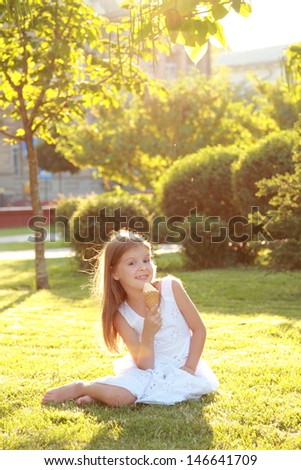 Happy cute little girl in casual clothes eat ice cream on a background of nature