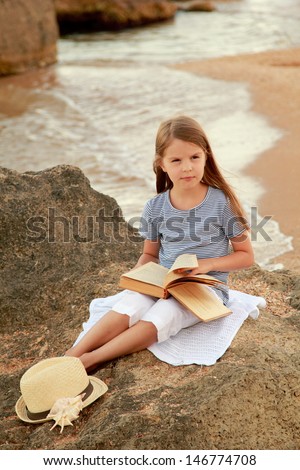 outdoor image of pretty little girl reading book near the ocean