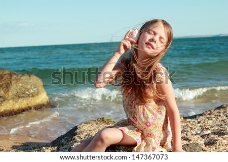 Adorable happy little girl holding a seashell on the sea beach on a sunny day