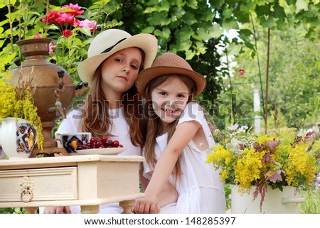 Adorable little girl drinking tea from an antique Russian samovar in the summer garden in the street / Russian antiques and national traditions