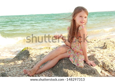 Charming joyful little girl in a summer dress dreaming and smiling at the beach