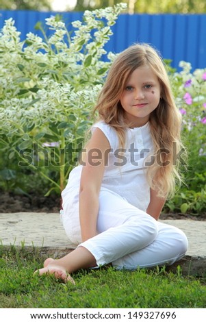 Portrait of a cute girl with long healthy hair in summer clothes walks in the yard on a background of green grass