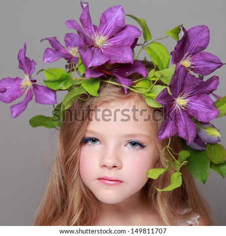 Close-up studio portrait of a beautiful little girl with a charming hair of purple clematis