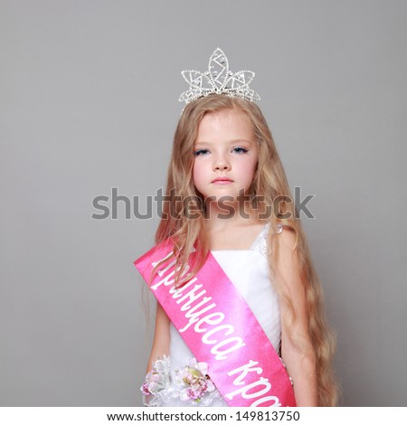 Young beautiful girl in a crown and a white dress won a beauty contest in Ukraine/ little girl in a white dress with a red ribbon and inscription in Ukrainian \