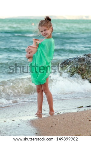 Adorable little girl in a green tunic holds ancient amphora/Little Greek goddess on the beach