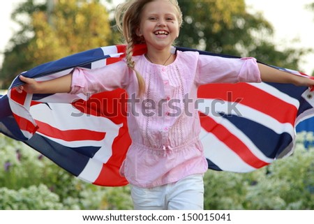 Cheerful beautiful young girl running with the flag of the UK in the summer garden