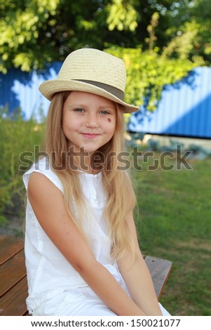 Portrait of a lovely little girl in a beautiful hat walks in the yard on a sunny day outdoor