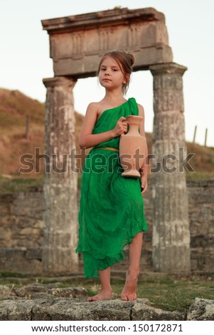 cute little girl in a bright emerald green dress standing in the ruins of the ancient city in the role of the Greek goddess