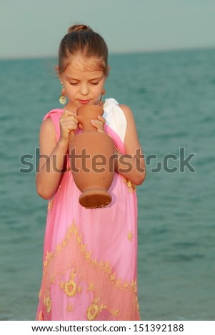 Greek goddess of the tender little dress with a beautiful hairstyle and ornaments sitting on the beach with an amphora/Girl like a goddess
