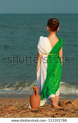 European cute girl holding a Greek-style amphora and dreams on the beach/Little girl in the role of the Greek goddess of outdoors
