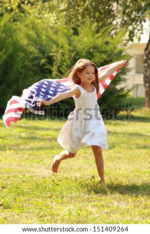 Beautiful joyful girl in a white dress holding a large American flag in a sunny summer day in the park