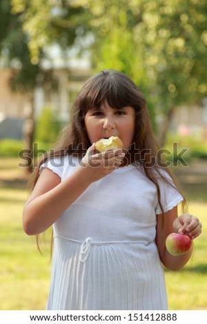 Lovely fat girl with a sweet smile and long brown hair holding a picnic basket and eating an apple in a sunny summer day