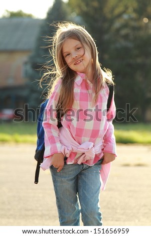Cute smiling schoolgirl in casual clothes with a backpack goes to school outdoors on Education