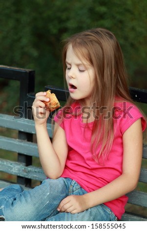Positive child sitting on a park bench and eating a pie