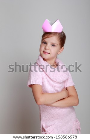 Portrait of charming smiling child in a pink knitted dress with a pink crown on his head on a gray background