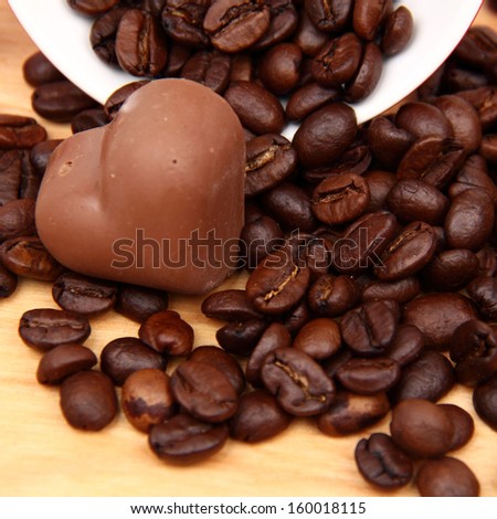 Coffee beans in red ceramic coffee cup with heart symbol and yummy chocolate heart on wooden desk