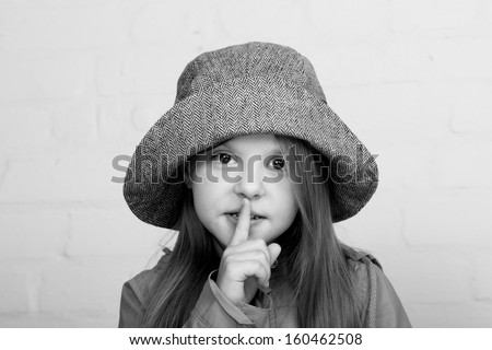 Little girl looking ahead and putting her finger to her lips/Black and white image of a beautiful little girl in a hat put a finger to his lips, showing a sign of silence
