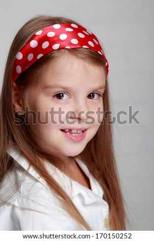 Portrait of lovely cheerful young girl with beautiful hair of red ribbon with polka dots on a gray background