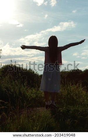 Silhouette little girl with open arms wide open on sky background at twilight