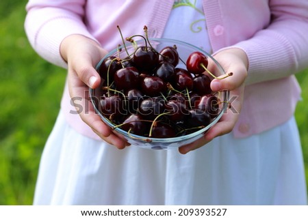 Children\'s hands holding a glass bowl full of cherries outdoor