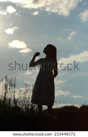 Silhouette little girl with open arms wide open on sky background at twilight