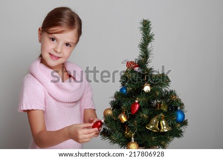 Studio image of a beautiful smiling little girl in a pink dress decorated Christmas tree in the New Year/Child near a decorated Christmas tree