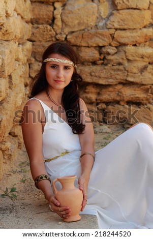 Attractive woman in white long dress in Greek style keeps ancient amphora background excavations of the ancient city as the ancient Greek goddess