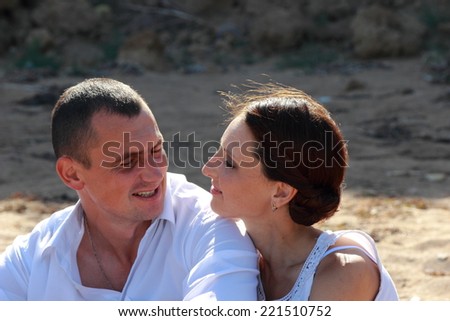 Embracing couple smiling at camera sitting on sand at the beach