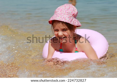 Funny little girl swims in a sea in a pink life preserver